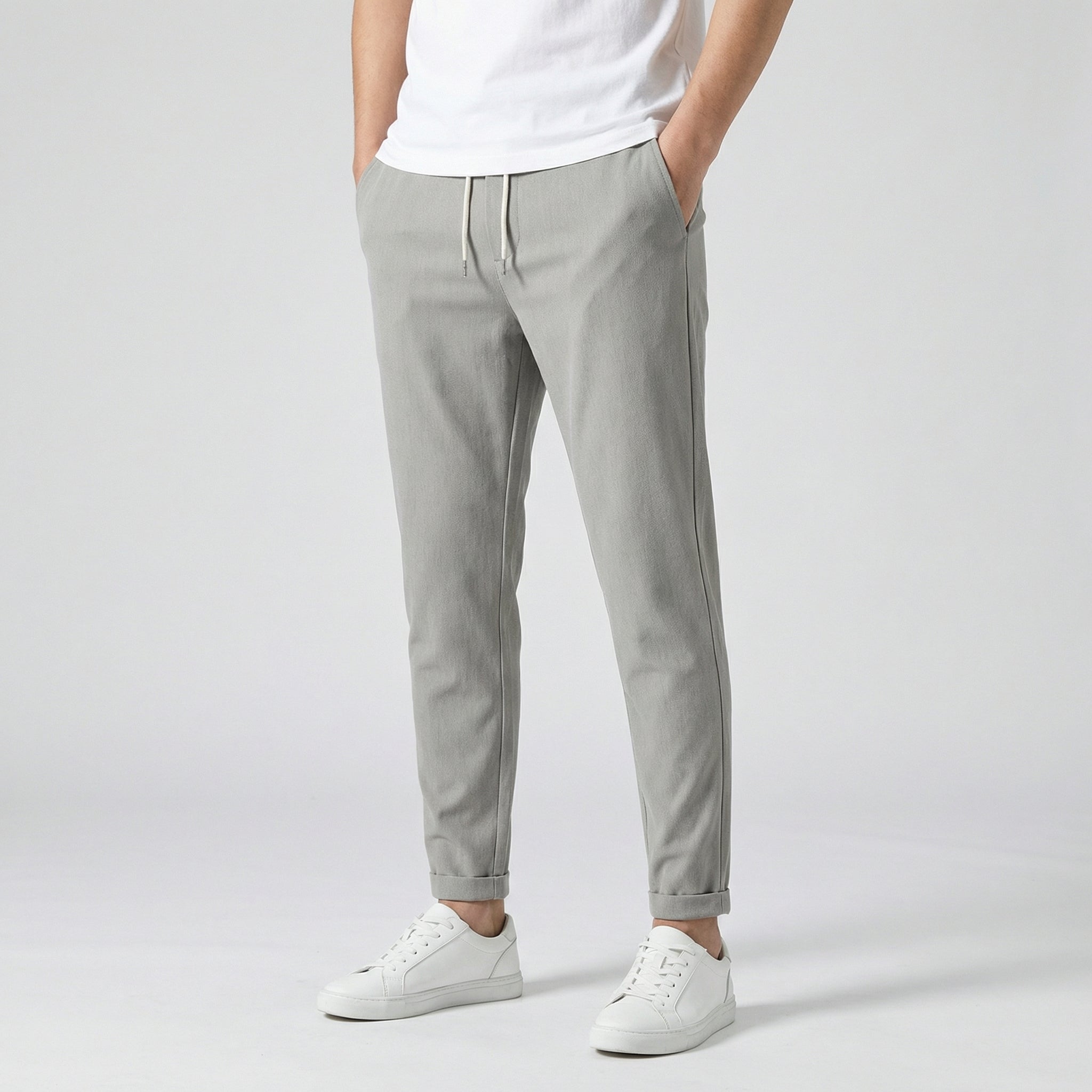 Pantalon jogger slim gris clair avec cordon de serrage blanc, porté par un homme en t-shirt blanc et baskets blanches