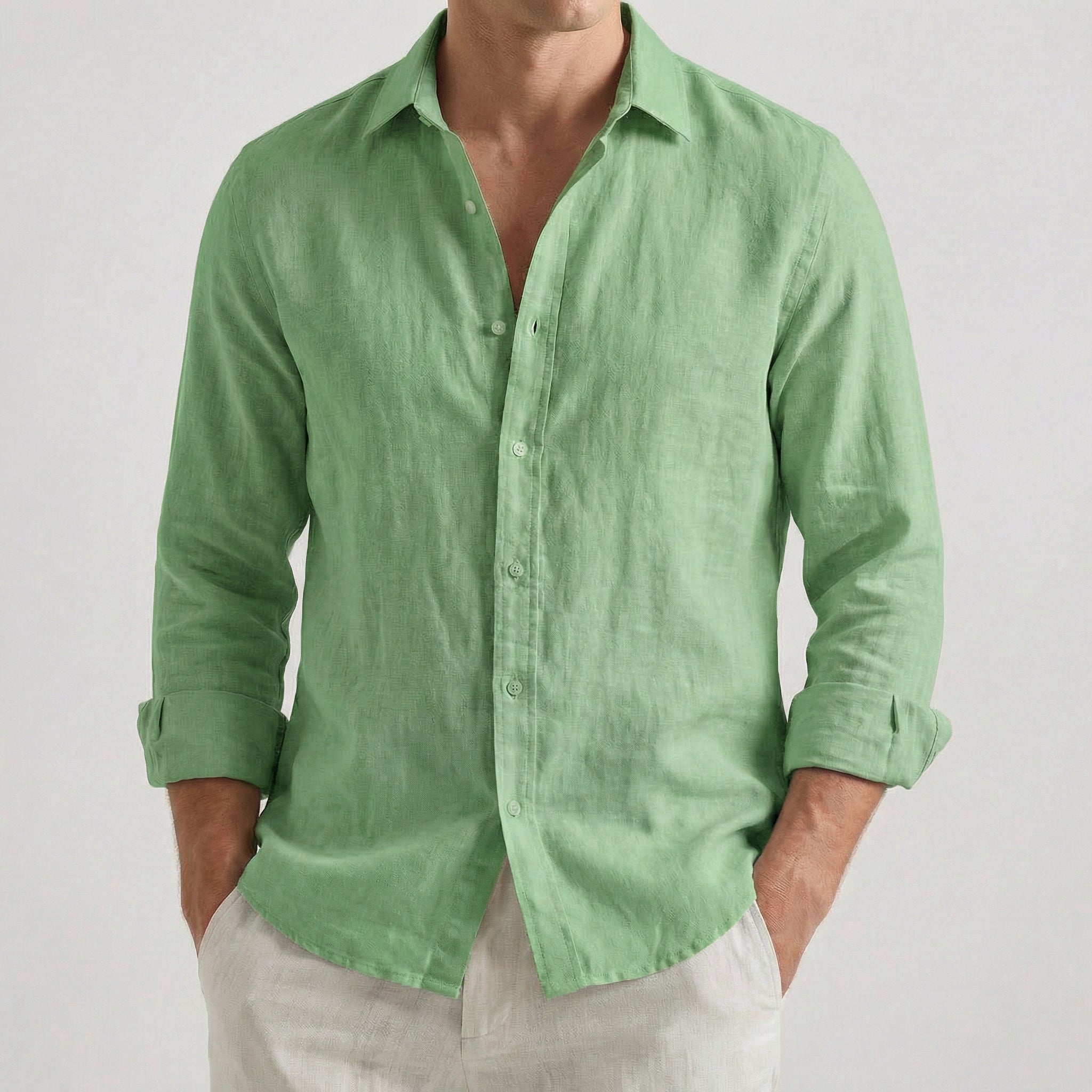 Chemise homme en lin à manches longues et col rabattu, coloris vert clair, portée par un mannequin masculin dans une pose décontractée sur fond gris clair