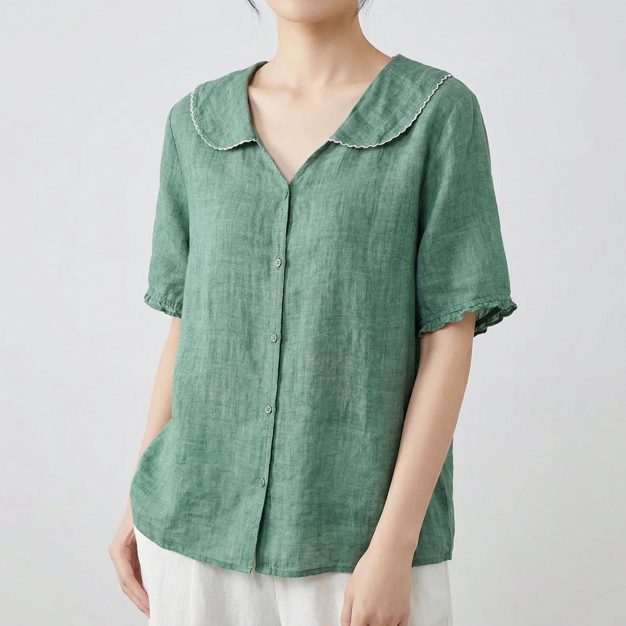 Chemise femme en lin à col chemisier et manches courtes en vert sauge, portée avec un pantalon blanc
