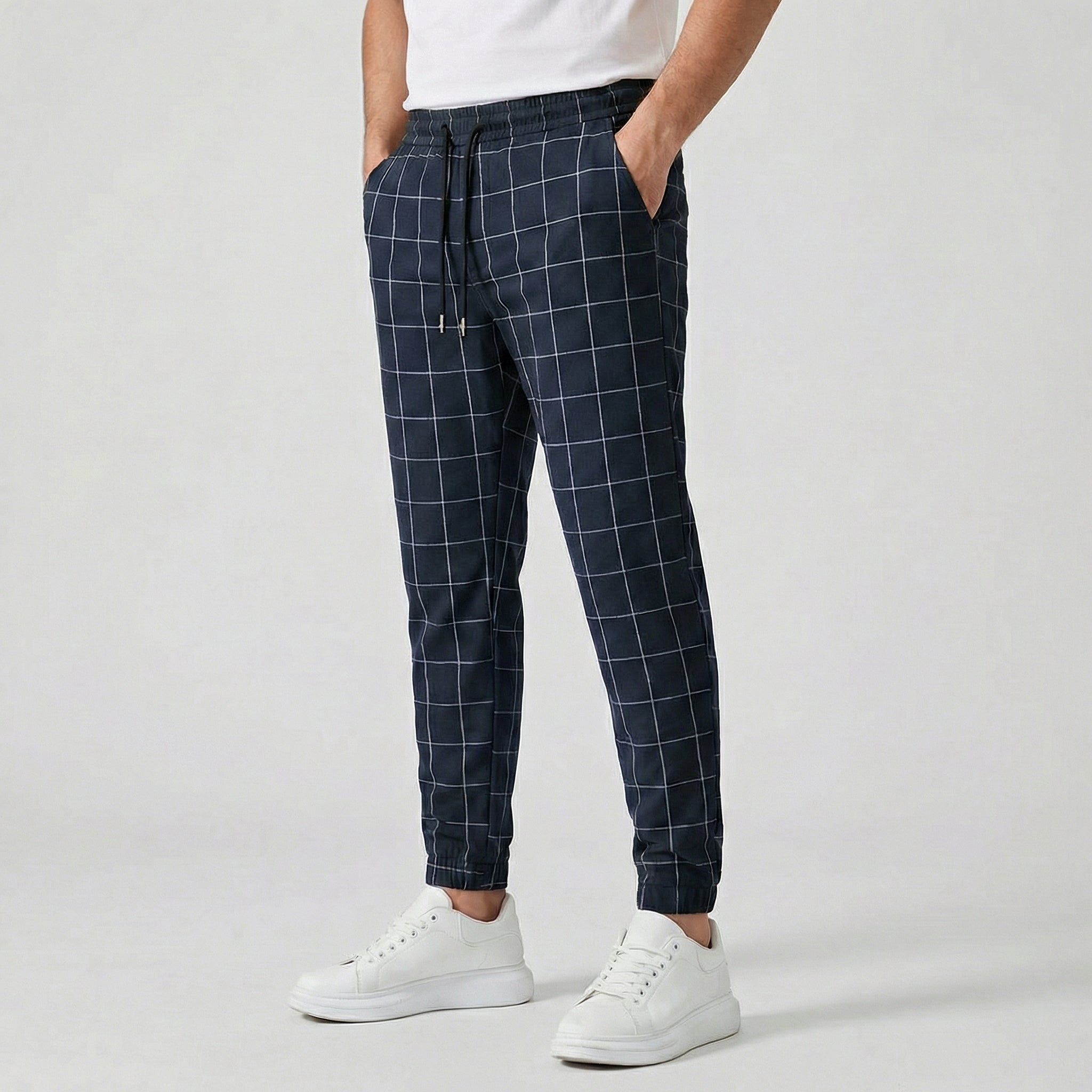 Pantalon jogger à carreaux pour homme, couleur bleu, taille élastiquée avec cordon, poches latérales et chevilles côtelées, porté avec des baskets blanches