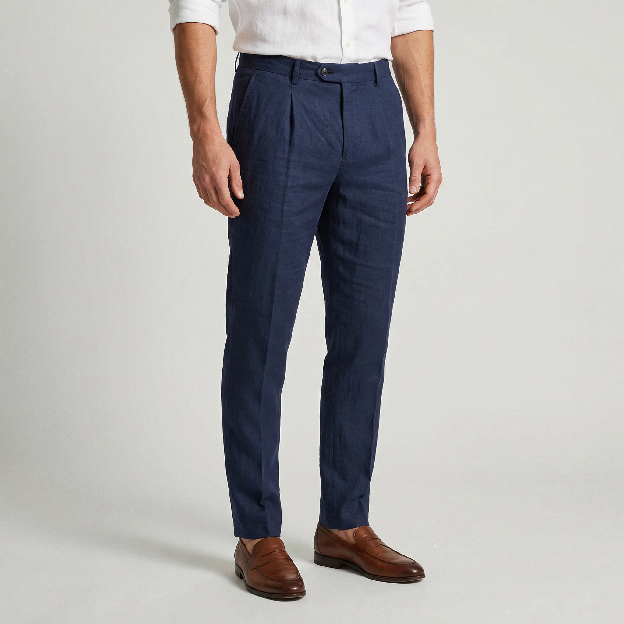 Pantalon en lin bleu marine à pinces, coupe slim effilée, porté avec une chemise blanche et des mocassins en cuir marron.