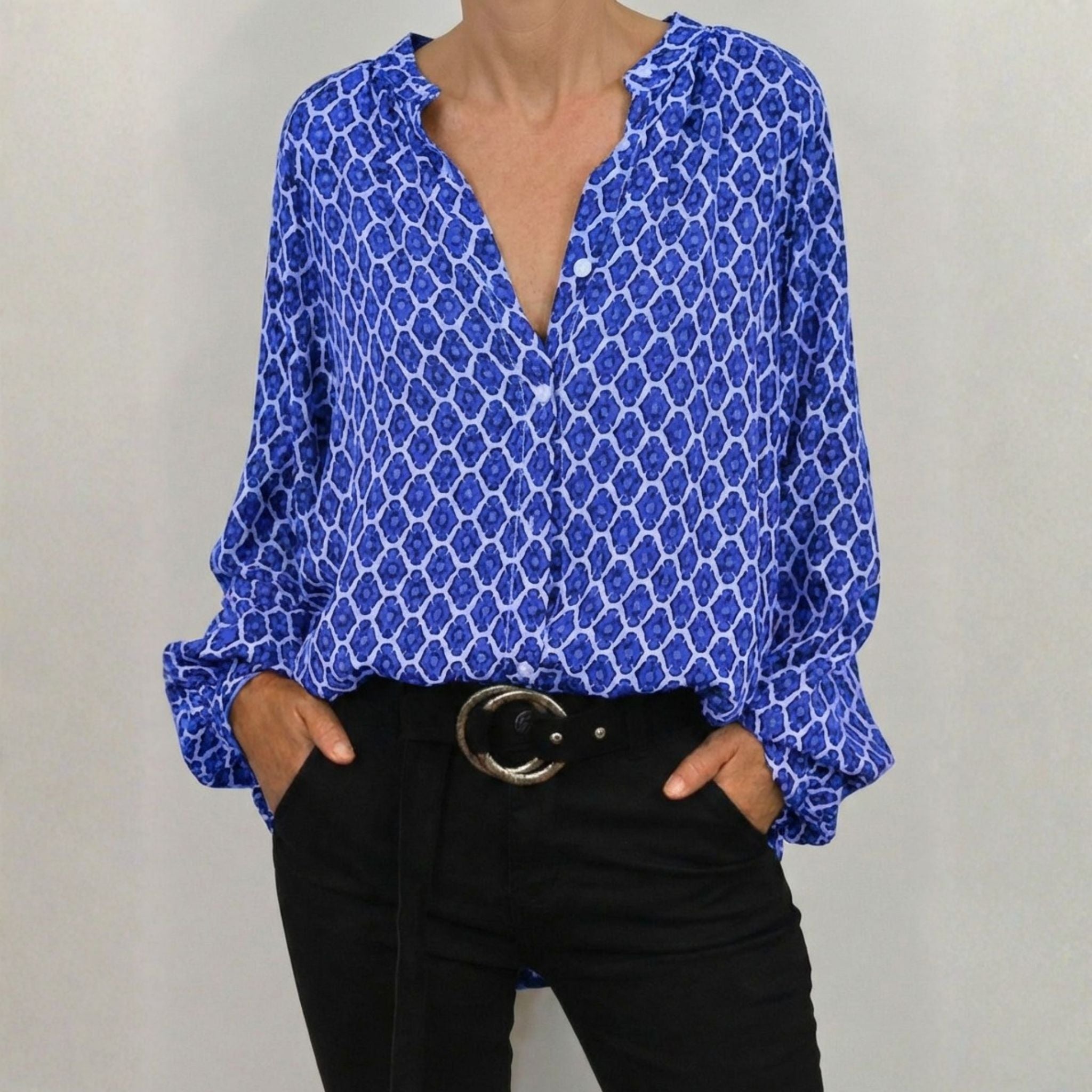 Blouse femme à motif géométrique bleu et blanc, col en V, manches longues avec poignets boutonnés, portée avec un pantalon noir et une ceinture noire