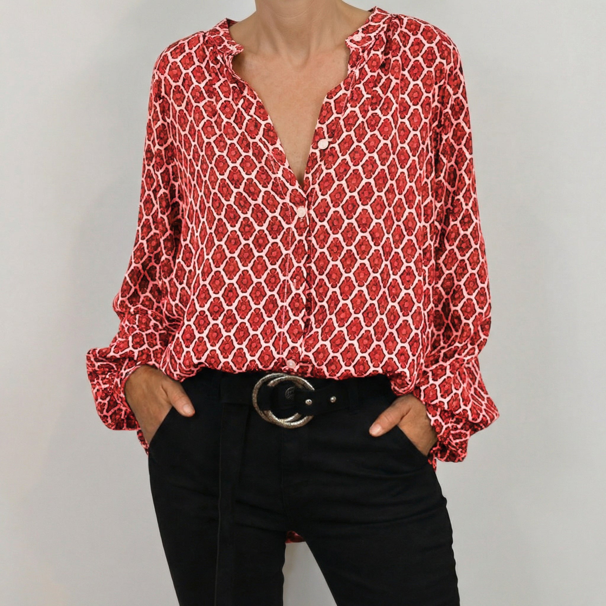 Blouse femme à motif géométrique rouge et blanc, col en V, manches longues avec poignets boutonnés, portée avec un pantalon noir et une ceinture noire