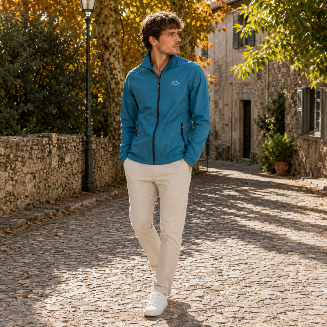 Blouson bleu pétrole ouvert au col, zip intégral visible, associé à un pantalon beige