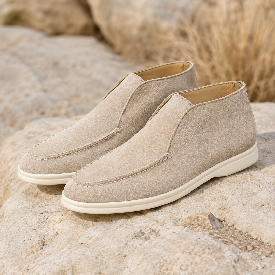 Bottines mocassins beiges à enfiler, couture apparente et semelle blanche, posées sur une roche