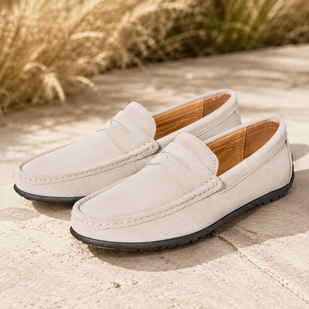 Mocassins homme blanc cassé au toucher velouté, semelle noire à picots sur pierre claire.