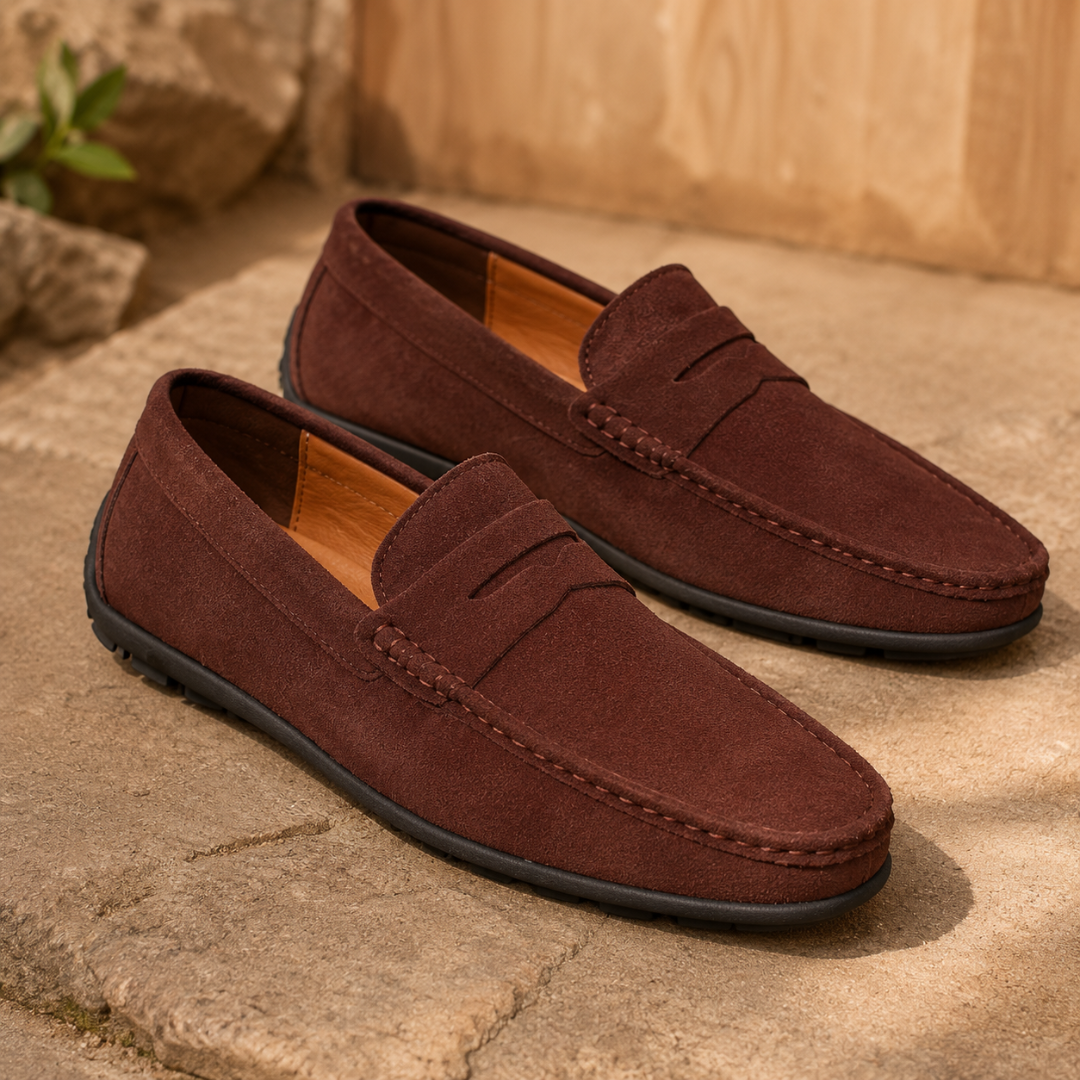 Mocassins homme marron foncé à bande penny, semelle sombre, posés sur des marches en pierre.