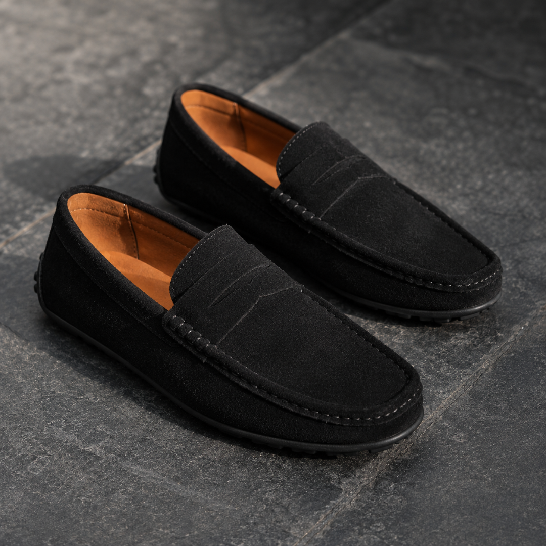 Mocassins homme noir mat à bande penny, semelle à picots, sol en ardoise sombre.