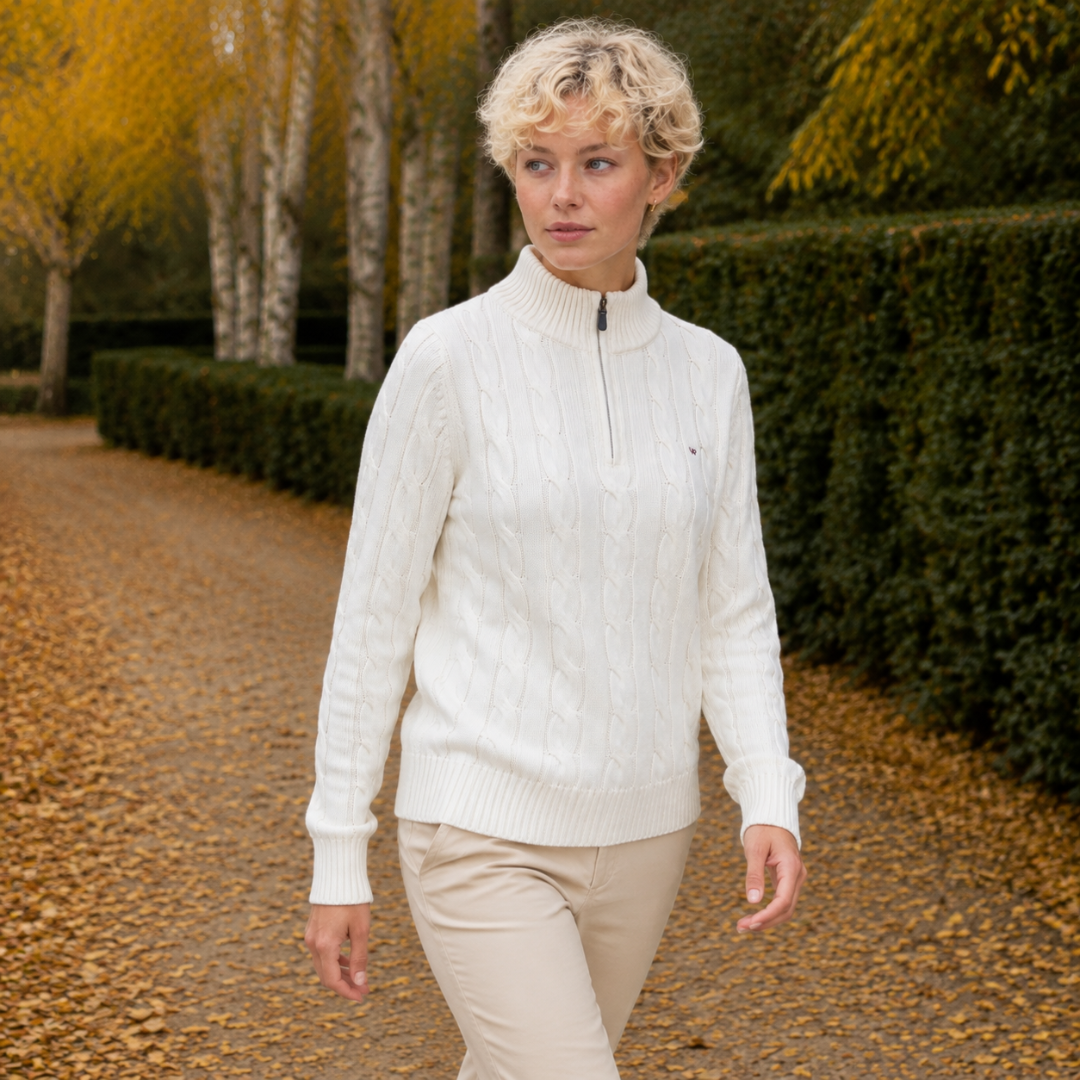 Femme marchant en pull blanc demi-zip, torsades verticales sur les manches longues et poignets côtelés