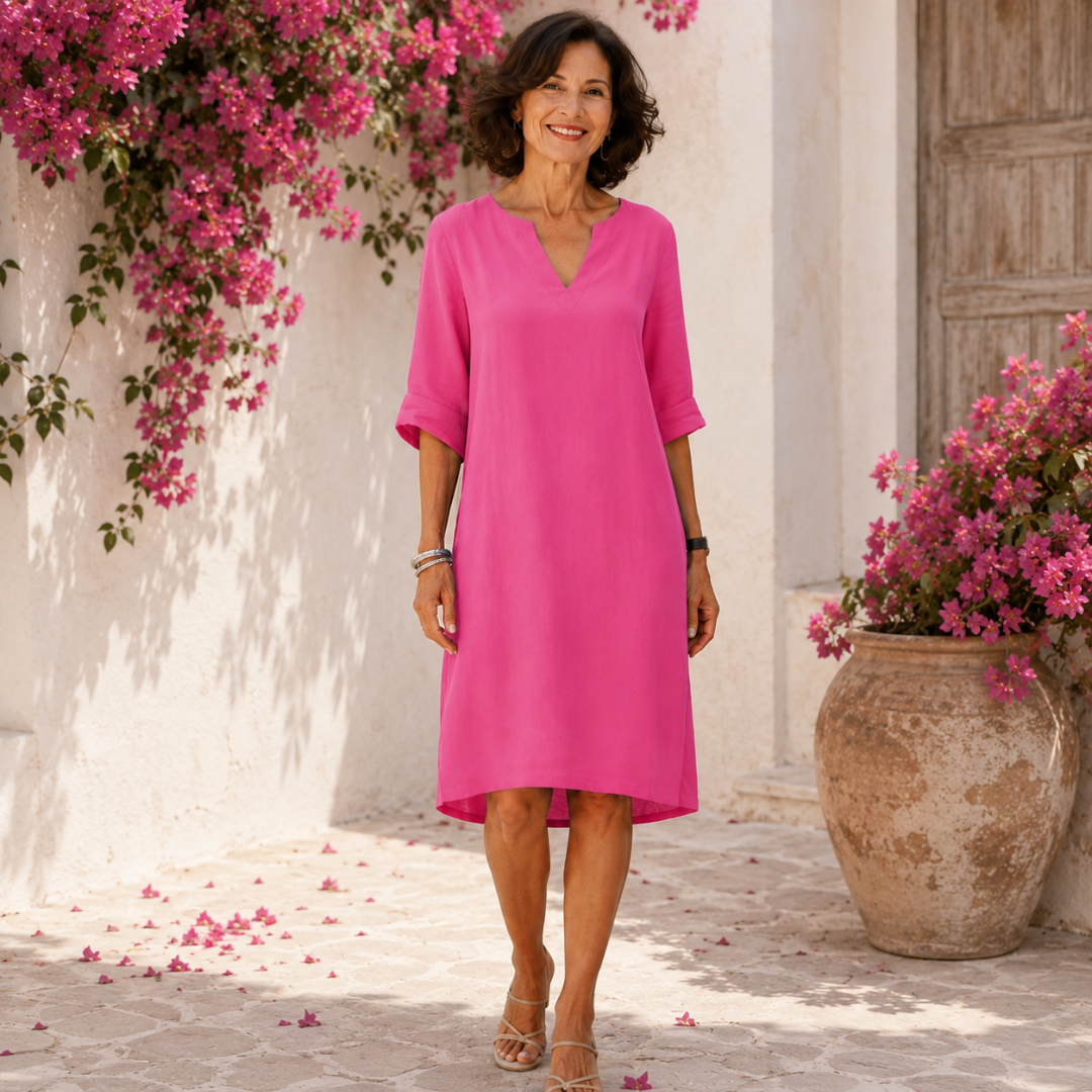 Robe femme mi-longue rose vif à col V portée devant un mur fleuri