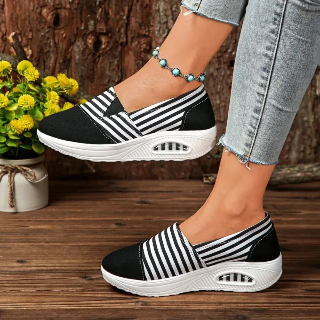 Vue latérale chaussure slip-on noire à rayures blanches sur sol en bois