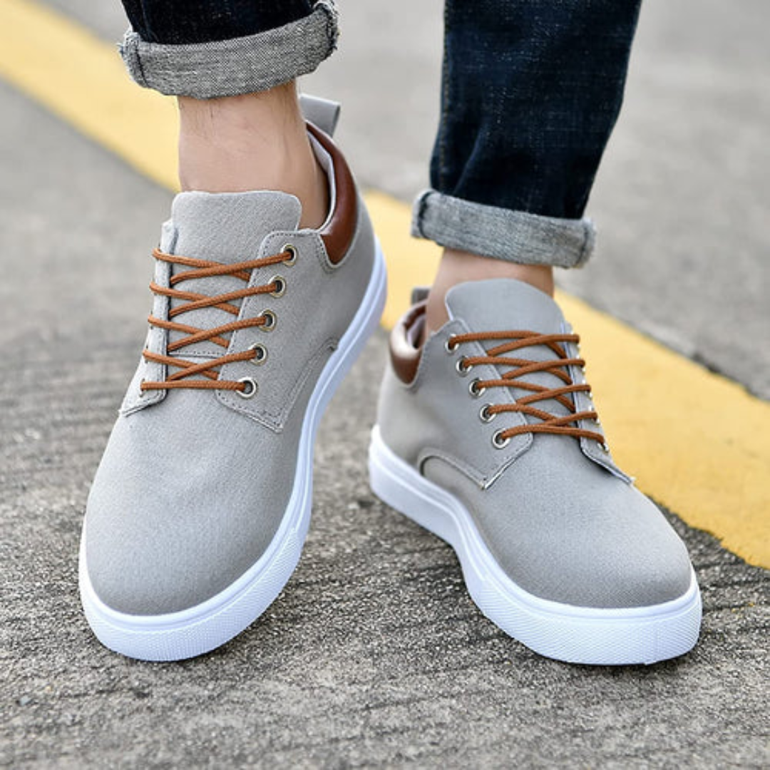 Paire de sneakers gris posée au sol, semelle blanche visible