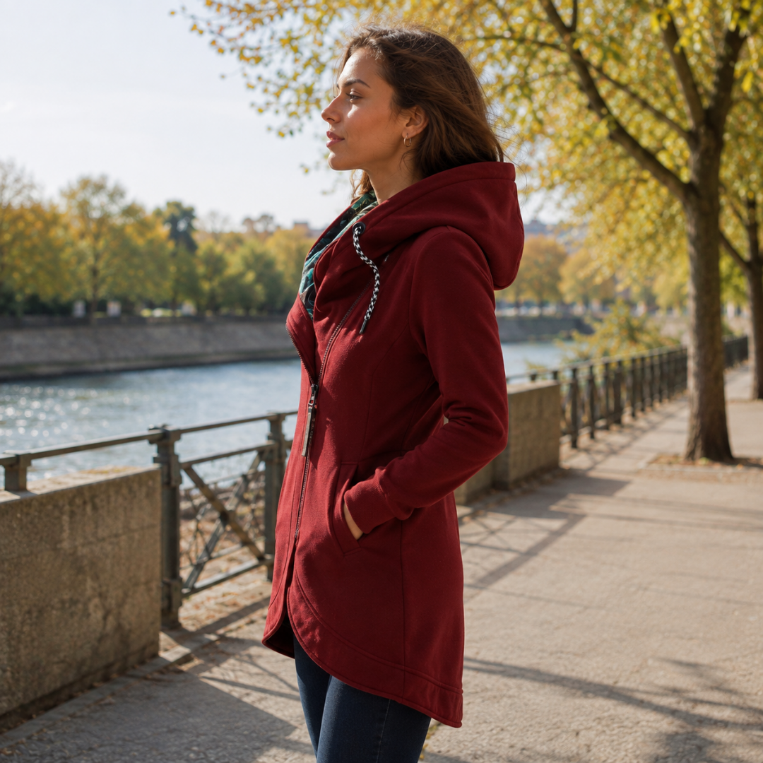 Veste longue rouge à capuche vue de profil, zip asymétrique et poche passepoilée