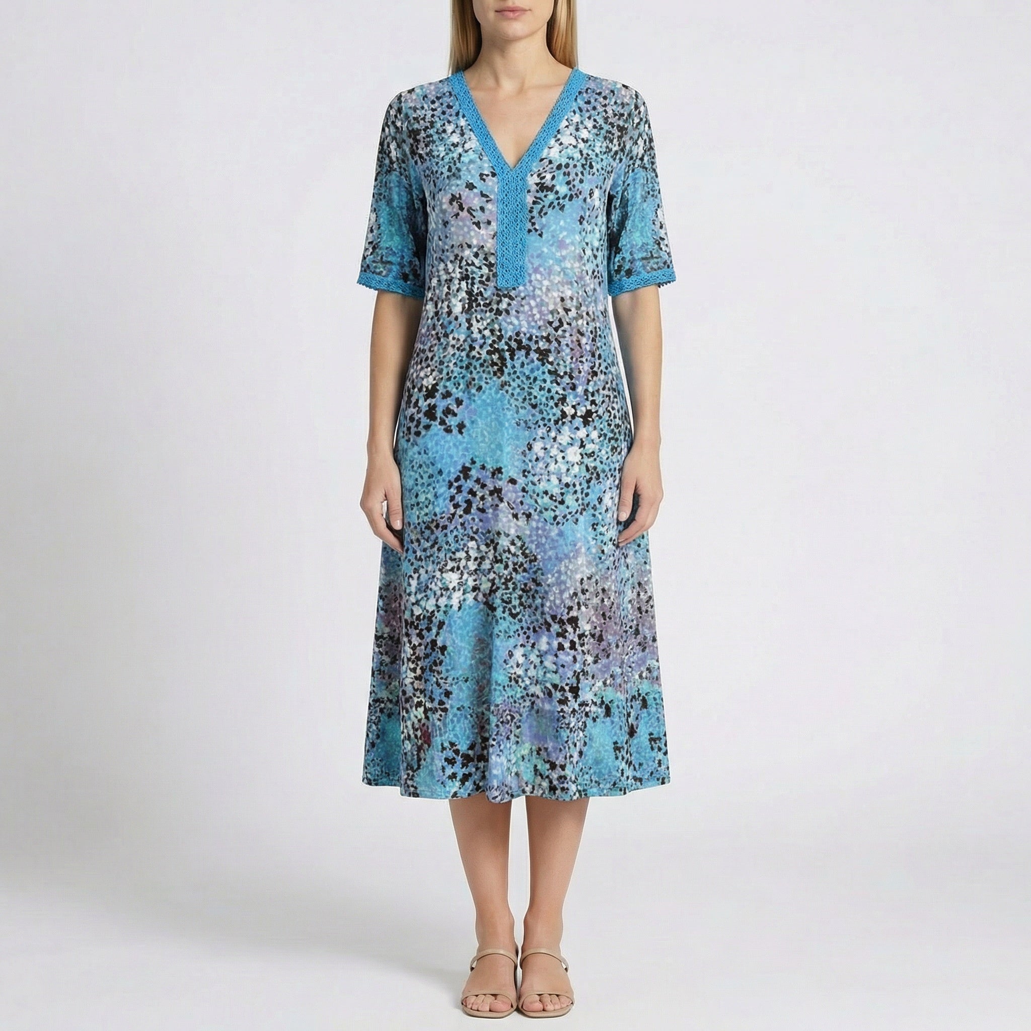 Robe midi Flore Bleu à col en V, détails en dentelle et imprimé floral abstrait en bleu, turquoise, violet et noir, portée par un mannequin sur fond gris clair