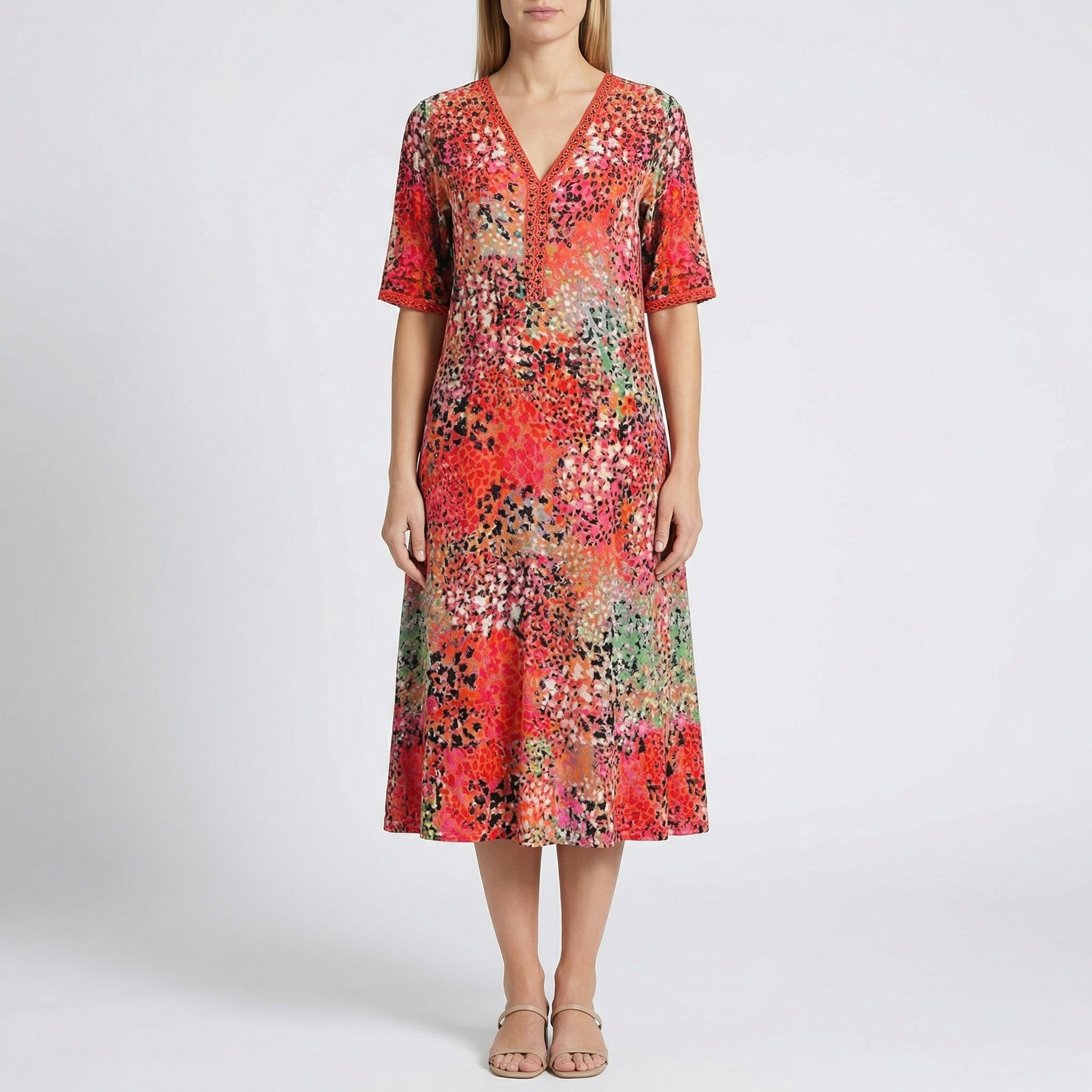 Robe midi Flore Rouge à col en V, détails en dentelle et imprimé floral abstrait en rouge, orange, rose et vert, portée par un mannequin sur fond gris clair