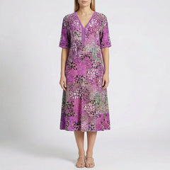 Robe midi Flore Violet à col en V, détails en dentelle et imprimé floral abstrait en violet, rose, vert et noir, portée par un mannequin sur fond gris clair
