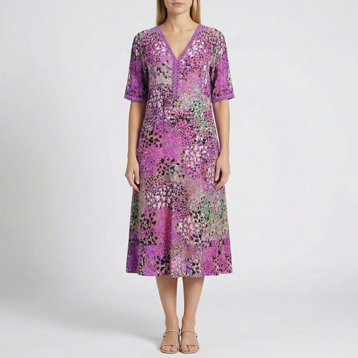 Robe midi Flore Violet à col en V, détails en dentelle et imprimé floral abstrait en violet, rose, vert et noir, portée par un mannequin sur fond gris clair
