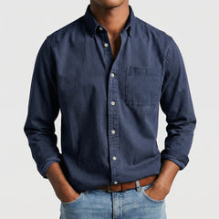 Chemise boutonnée manches longues en bleu marine, portée par un mannequin masculin sans visage visible, pose décontractée, fond gris clair