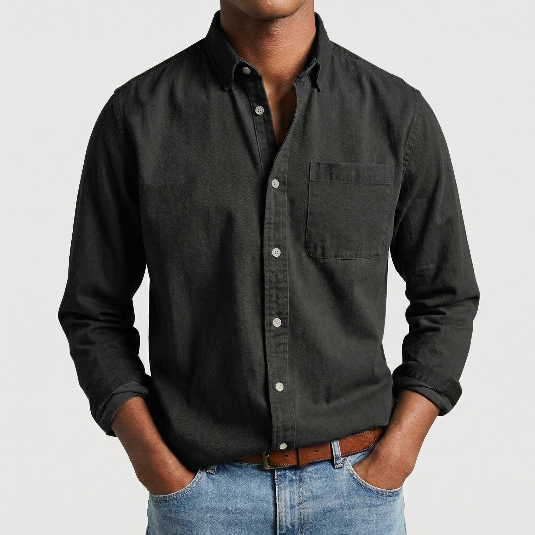 Chemise boutonnée manches longues en noir, portée par un mannequin masculin sans visage visible, pose décontractée, fond gris clair