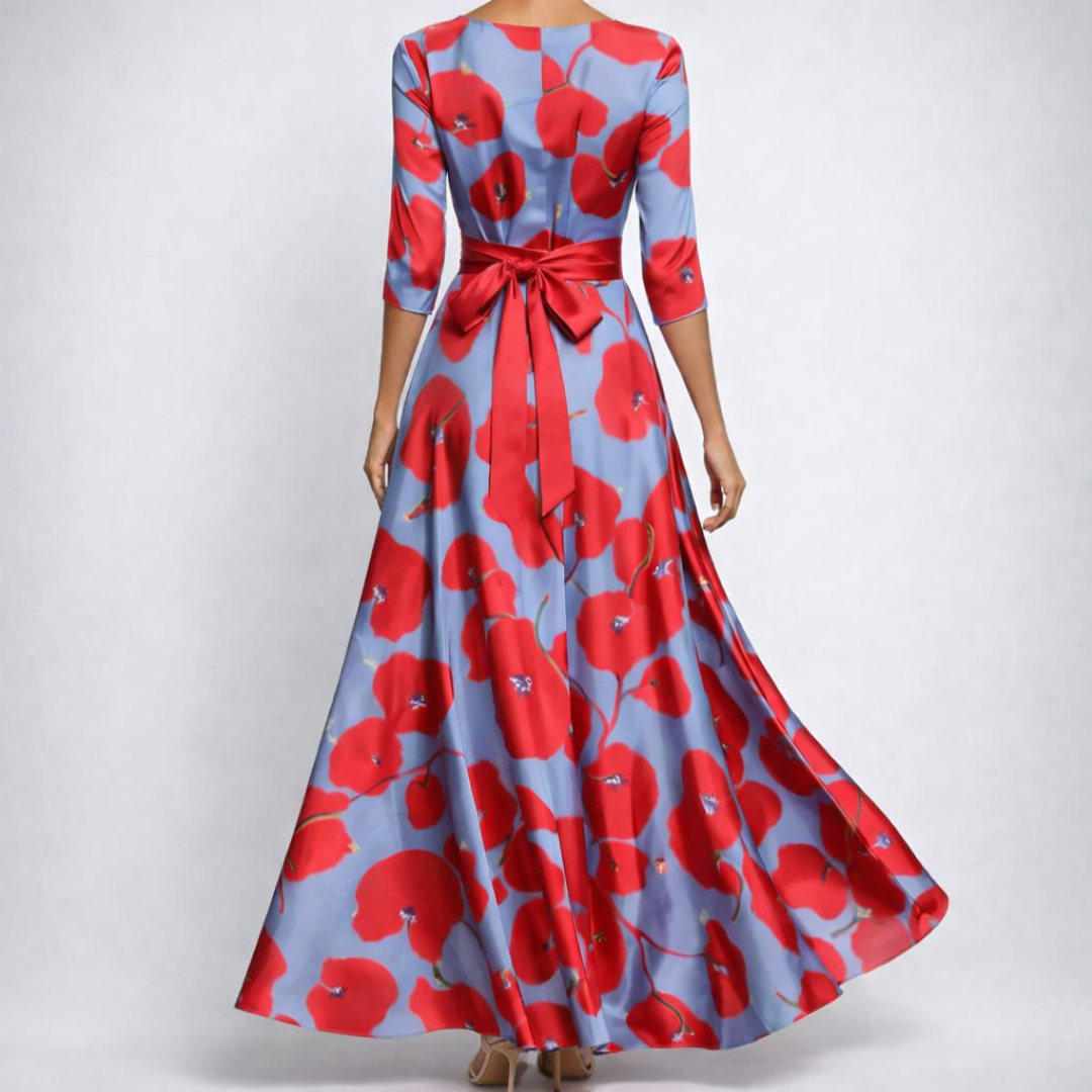 Robe maxi portefeuille à manches 3/4, fond bleu-gris avec grand imprimé coquelicot rouge et rose vif, col V croisé, nœud à la taille, jupe évasée vue de face

