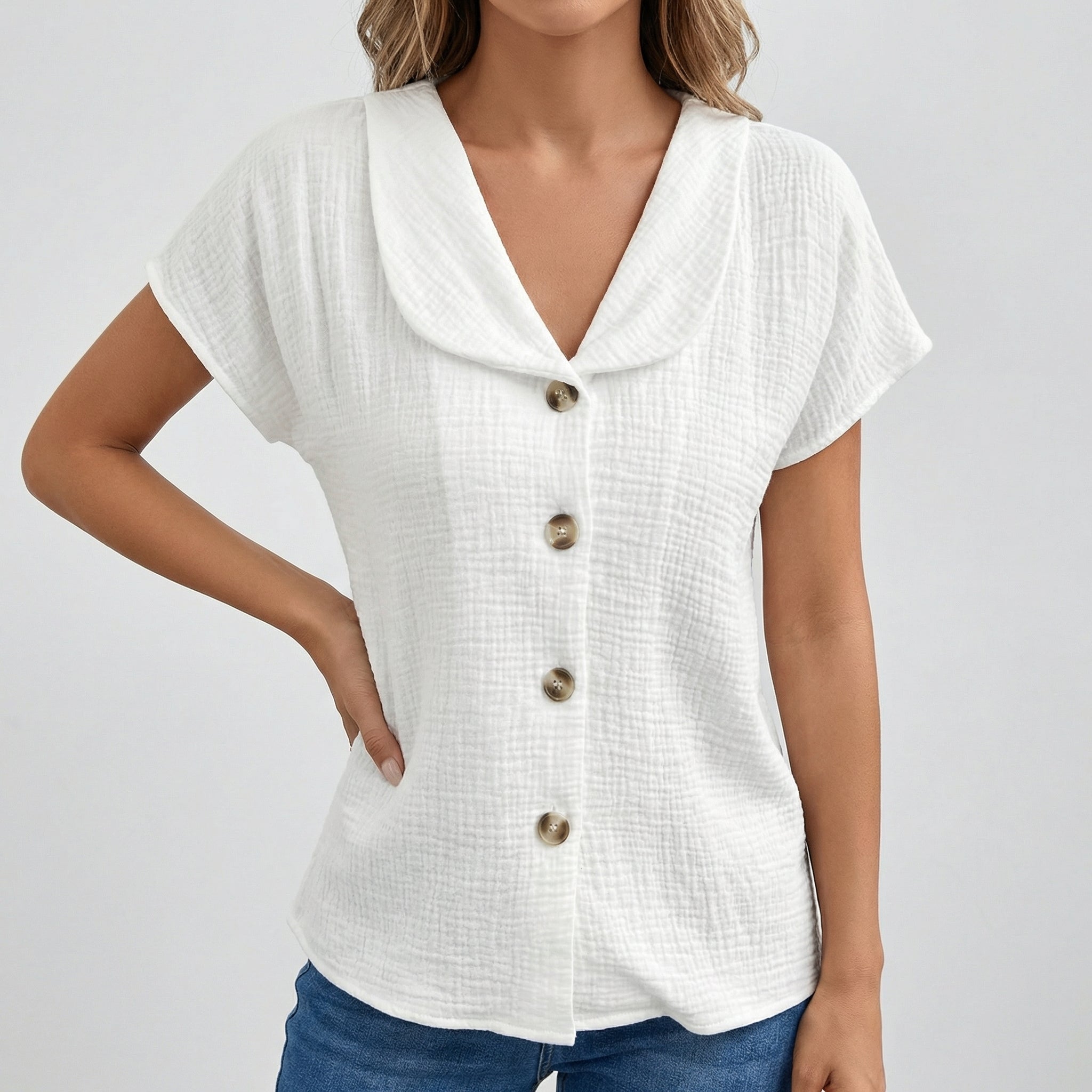 Blouse blanche à col rabattu, boutons dorés sur le devant, manches courtes, tissu gauze texturé, portée avec un jean bleu.