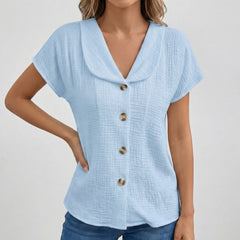 Blouse bleu clair à col rabattu, boutons dorés sur le devant, manches courtes, tissu gauze texturé, coupe décontractée