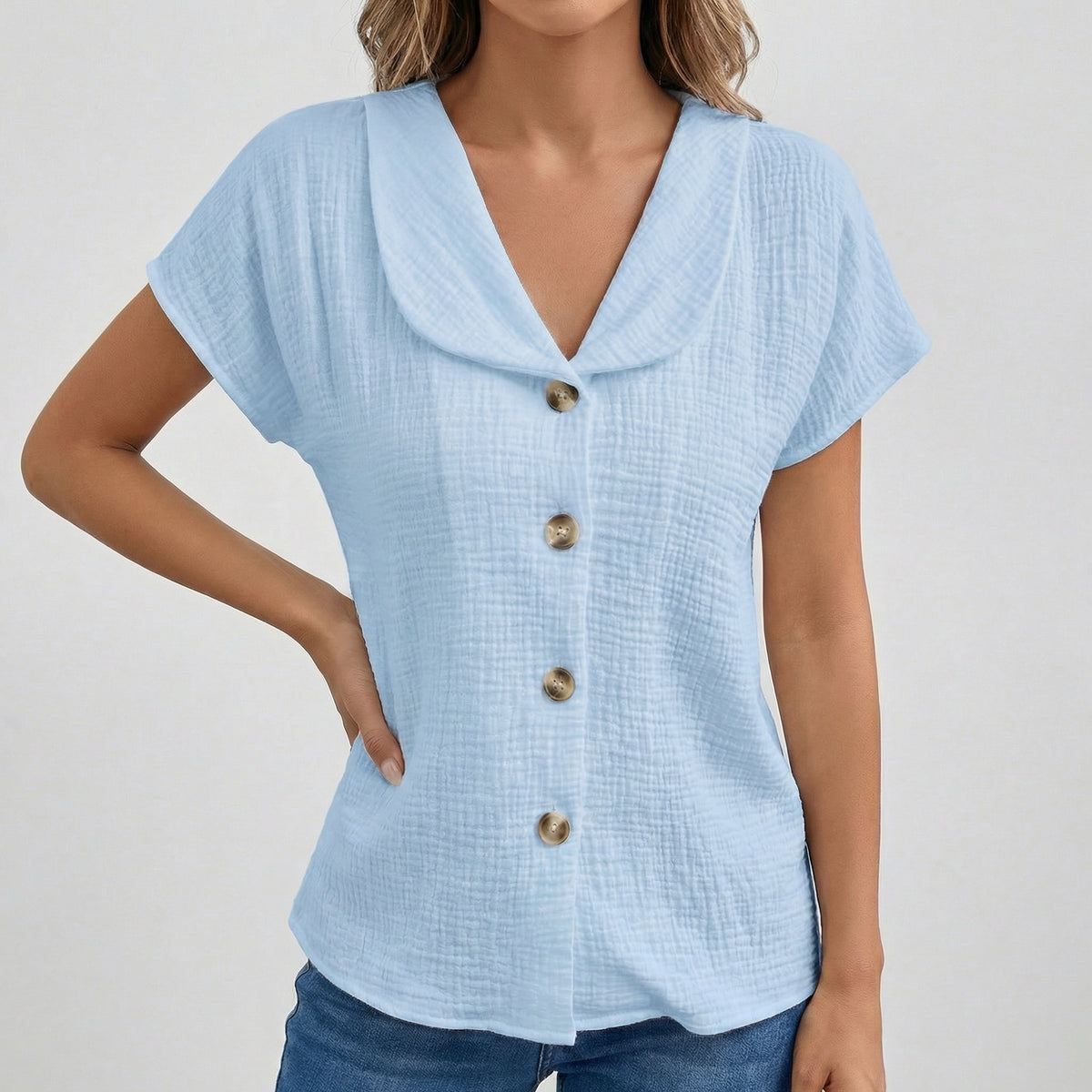 Blouse bleu clair à col rabattu, boutons dorés sur le devant, manches courtes, tissu gauze texturé, coupe décontractée
