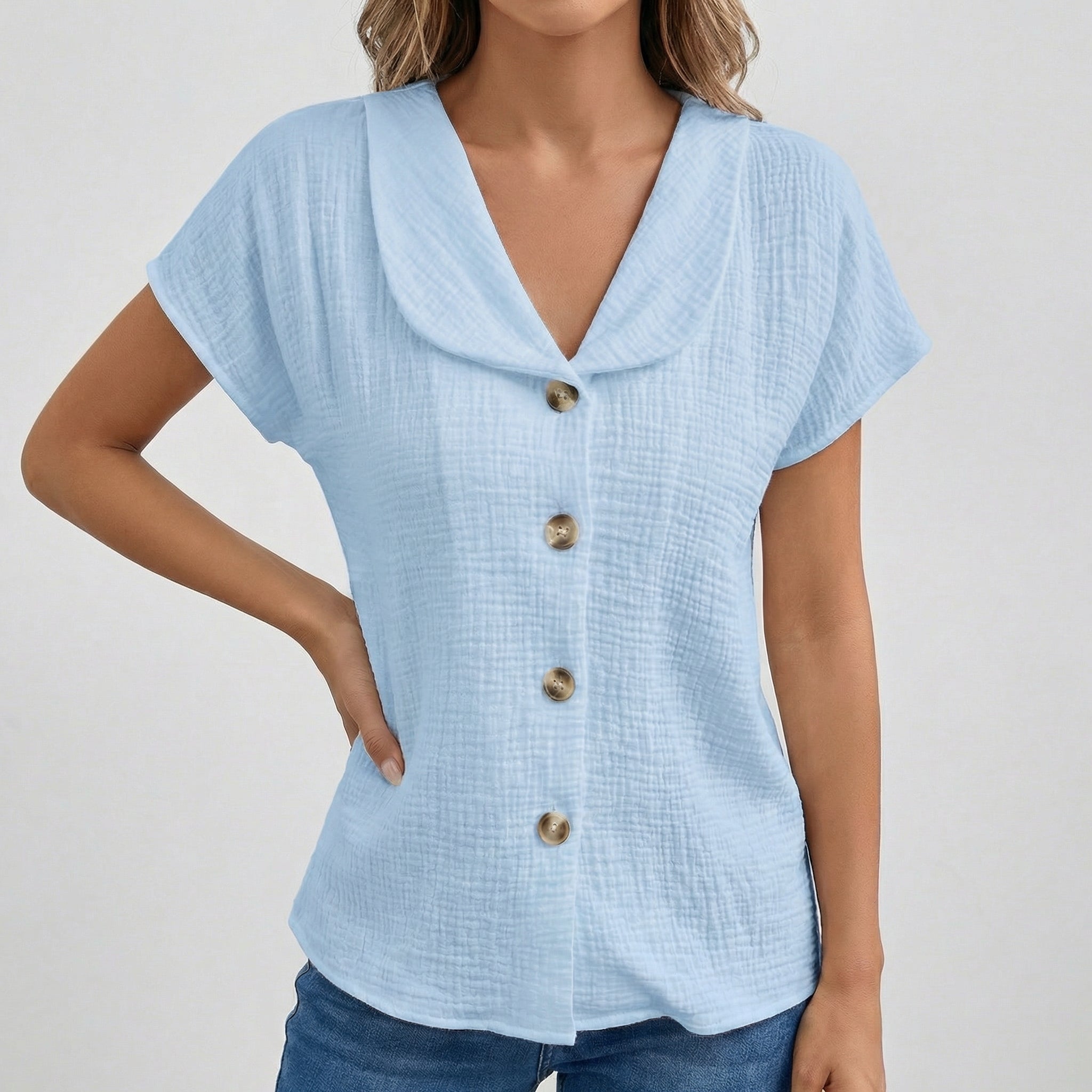 Blouse bleu clair à col rabattu, boutons dorés sur le devant, manches courtes, tissu gauze texturé, coupe décontractée