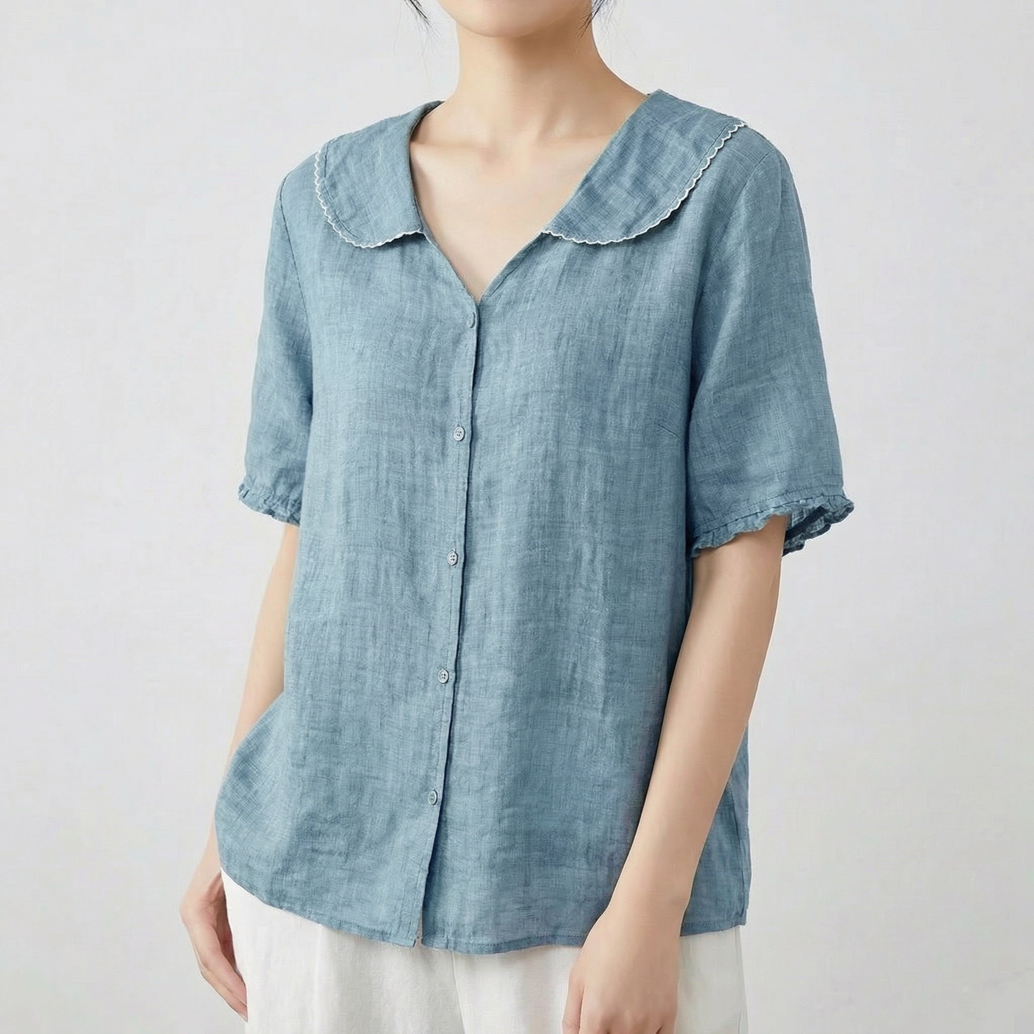 Chemise femme en lin à col chemisier et manches courtes en bleu grisé, portée avec un pantalon blanc