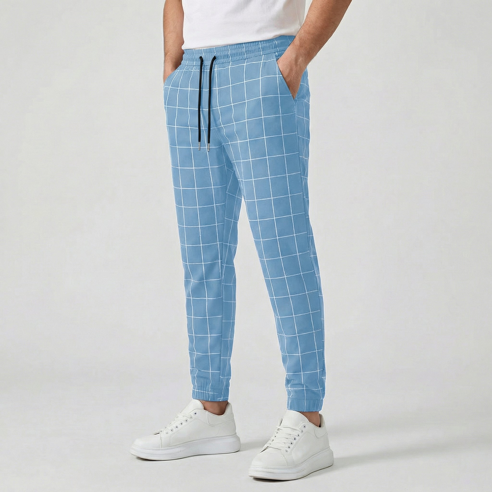 Pantalon jogger à carreaux pour homme, couleur bleu clair, taille élastiquée avec cordon, poches latérales et chevilles côtelées, porté avec des baskets blanches