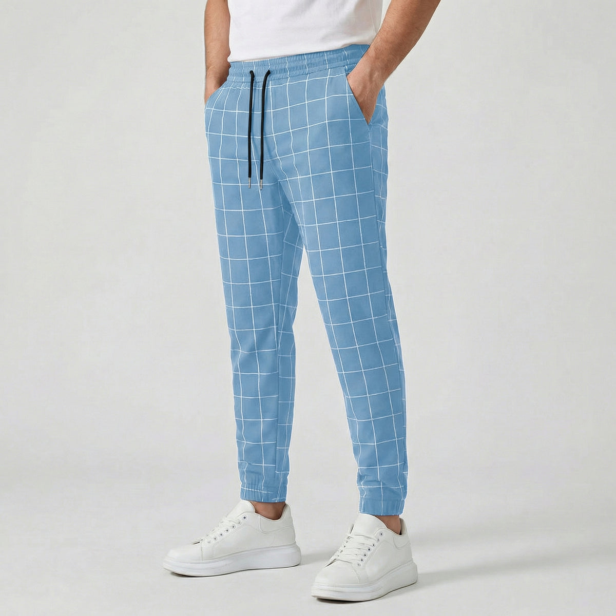 Pantalon jogger à carreaux pour homme, couleur bleu clair, taille élastiquée avec cordon, poches latérales et chevilles côtelées, porté avec des baskets blanches