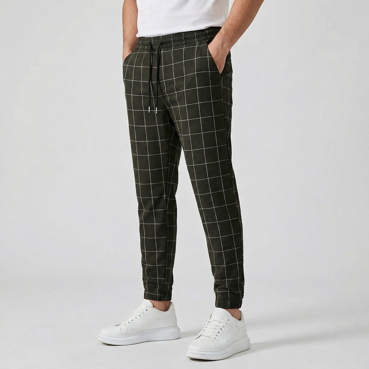 Pantalon jogger à carreaux pour homme, couleur noir, taille élastiquée avec cordon, poches latérales et chevilles côtelées, porté avec des baskets blanches