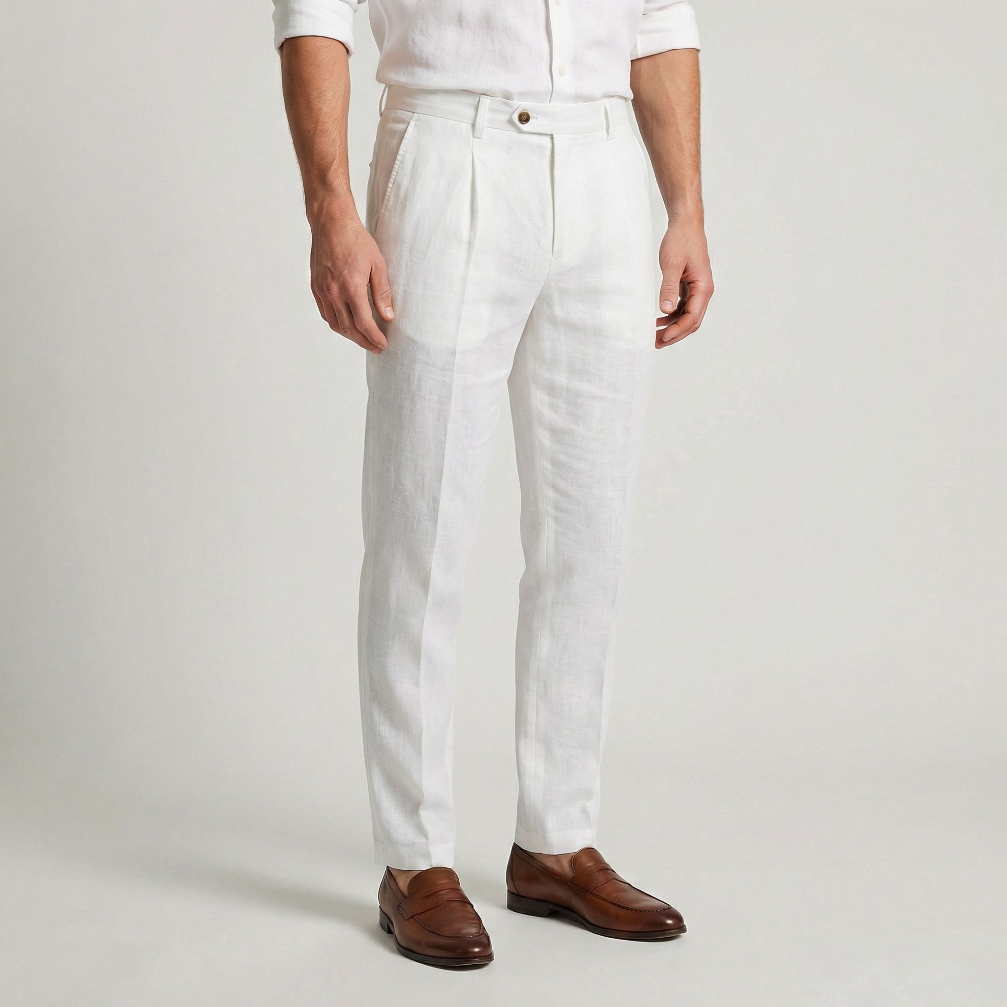 Pantalon en lin blanc à pinces, coupe slim effilée, porté avec une chemise blanche et des mocassins en cuir marron.

