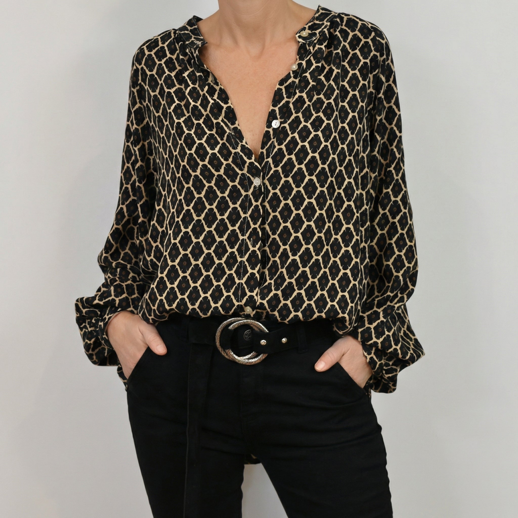 Blouse femme à motif géométrique noir et beige, col en V, manches longues avec poignets boutonnés, portée avec un pantalon noir et une ceinture noire