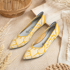 Ballerines jaunes et blanches à bout pointu et motifs graphiques posées sur une planche en bois