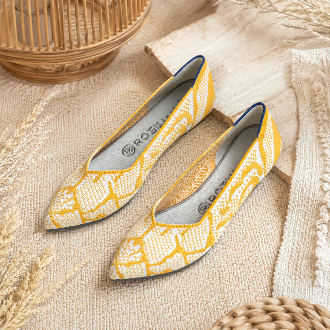 Ballerines jaunes et blanches à bout pointu et motifs graphiques posées sur une planche en bois