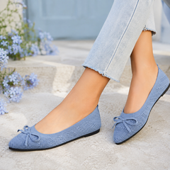 Ballerines bleu clair ajourées avec nœud fin, portées près de fleurs bleues