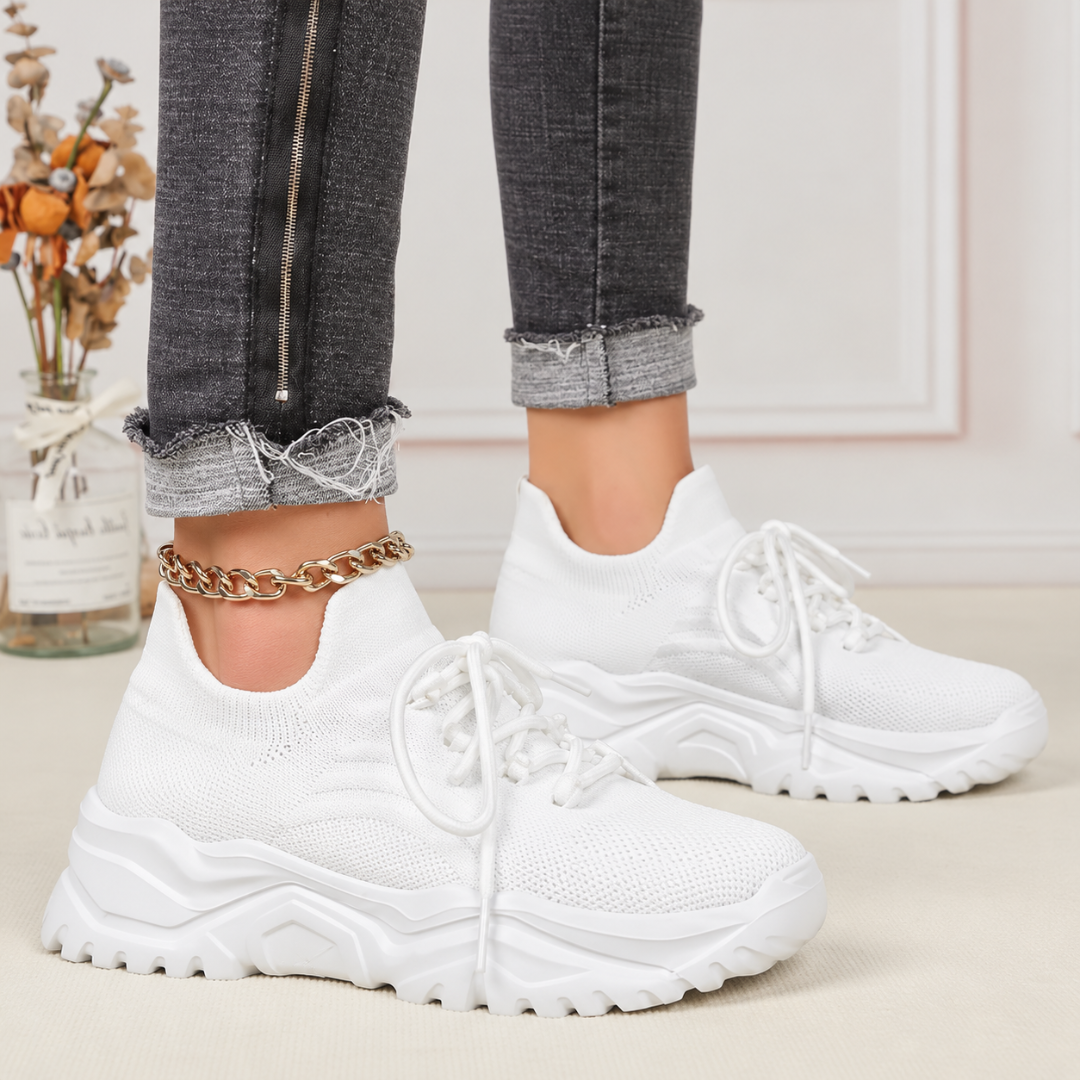 Baskets femme blanches portées avec un pantalon gris, laçage haut sur le pied