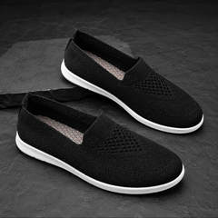 Baskets noires à enfiler sur pierre sombre, perforations discrètes et semelle blanche