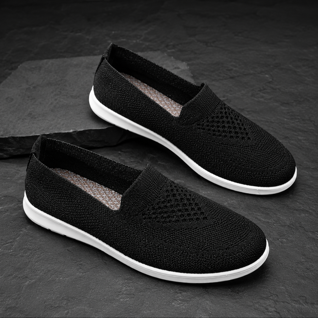 Baskets noires à enfiler sur pierre sombre, perforations discrètes et semelle blanche