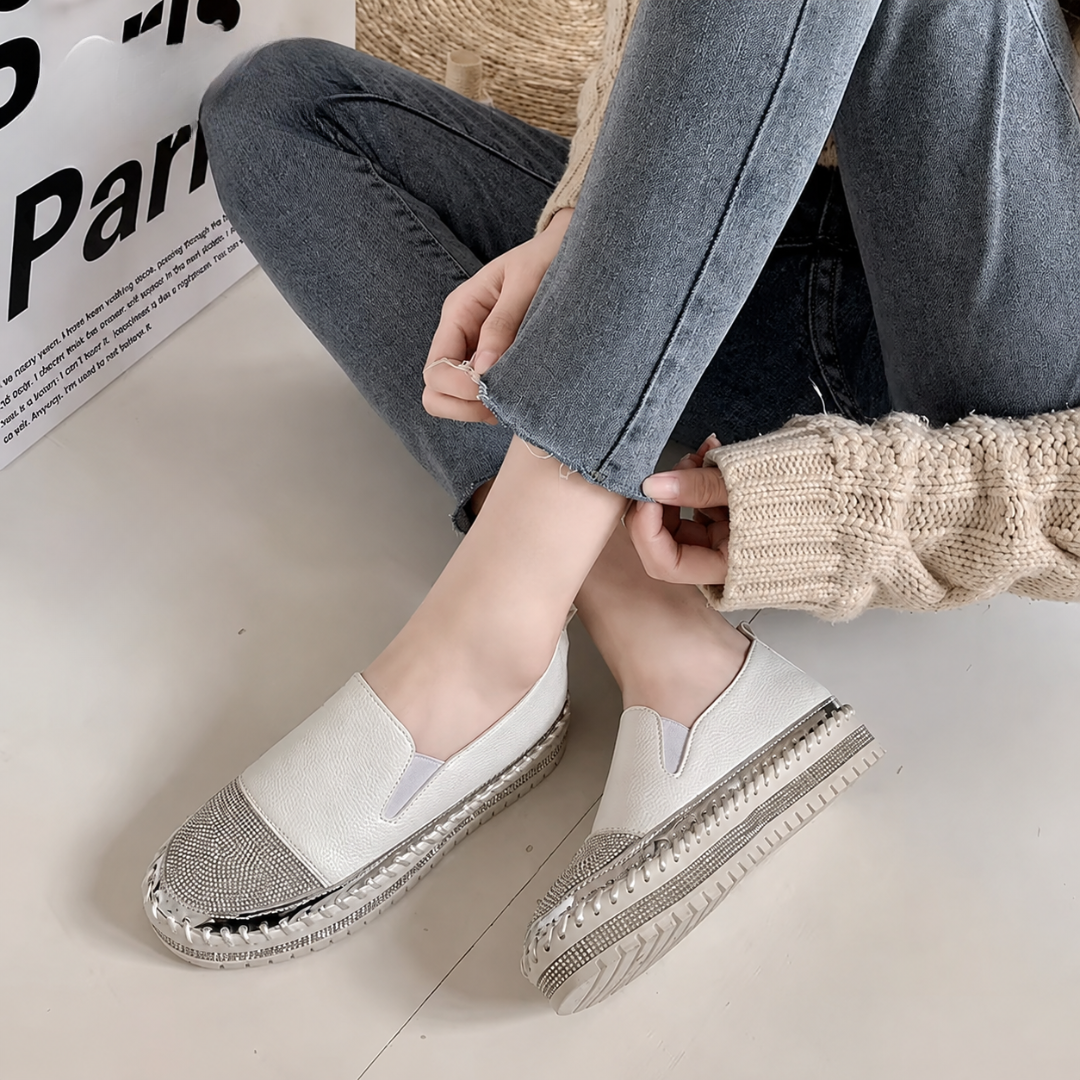 Baskets slip-on blanches portées avec un pantalon gris, plateforme crantée et surpiqûres visibles
