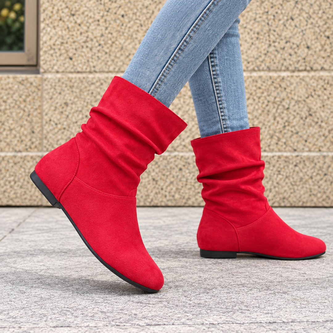 Bottes femme rouges drapées portées avec un pantalon bleu, talon plat et semelle sombre