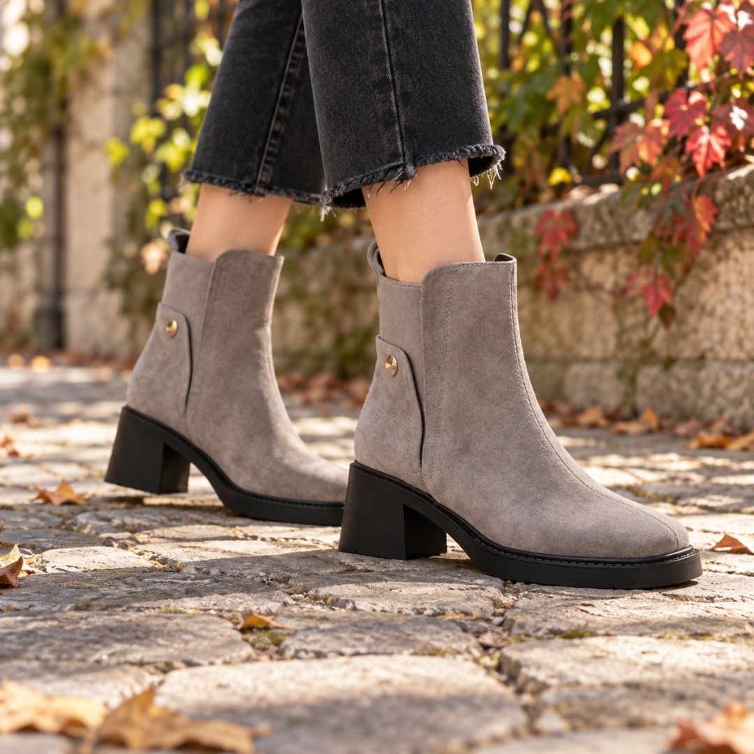 Bottines grises portées sur pavés, petit bouton doré sur le côté de la tige