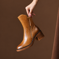 Bottine marron tenue à la main, zip doré ouvert et talon bloc