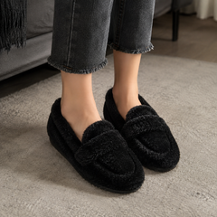 Chaussons femme noirs façon mocassin portés avec un pantalon gris, semelle plate