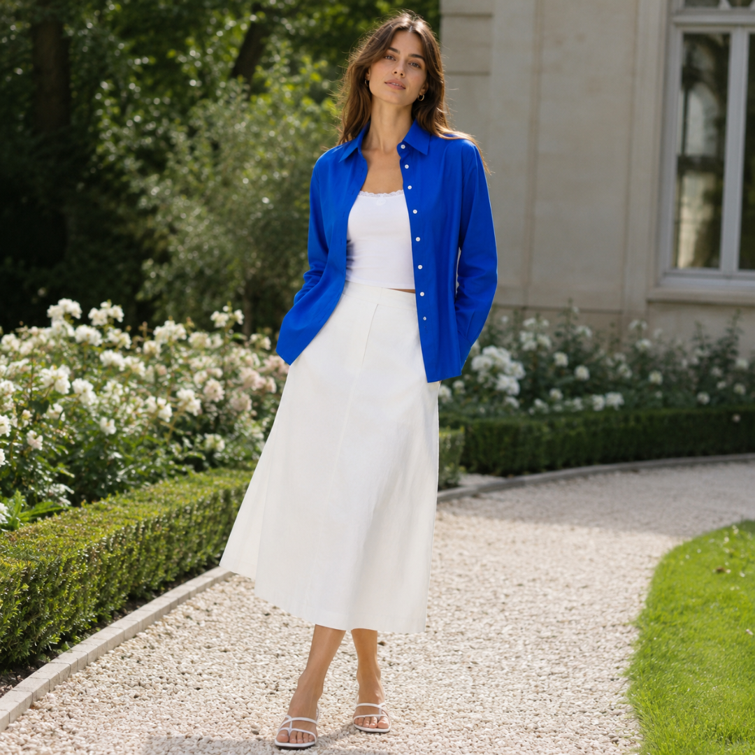 Chemise bleue ouverte sur un top blanc et une jupe longue, dans un jardin fleuri