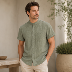 Homme en chemise vert olive col mao, mains dans les poches près d'une table en bois
