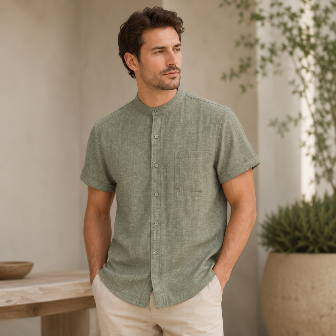Homme en chemise vert olive col mao, mains dans les poches près d'une table en bois