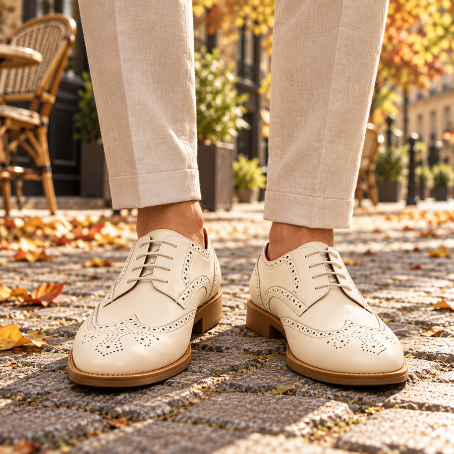 Derbies homme blancs à perforations brogue portés avec un pantalon beige retroussé
