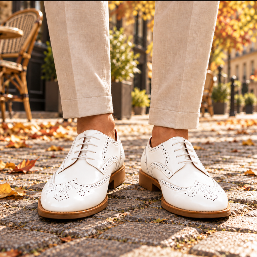Derbies homme blancs brillants à perforations brogue, portés sur pavés en automne
